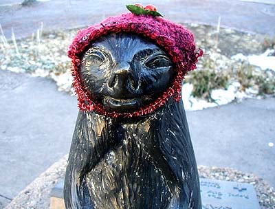 A metal groundhog in a hat speaking to St. Francis (St. Francis not shown, life-sized).