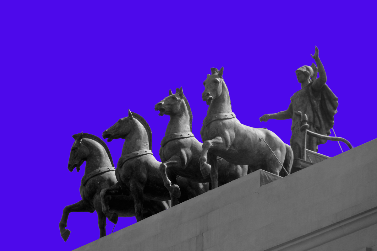 Image of a statue featuring four horses being led by a charioteer, against dark purple background.