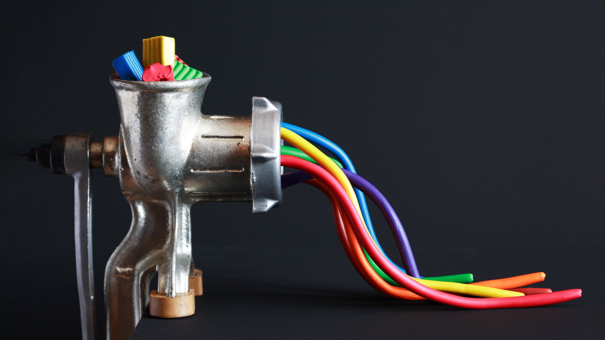 Image of colorful blocks of clay being put into a grinder, with similarly colorful wires of clay coming out.