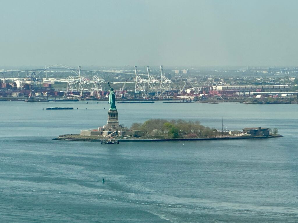 Photograph of New York Harbor and the coast of New Jersey with Liberty Island and the Statue of Liberty in the foreground.