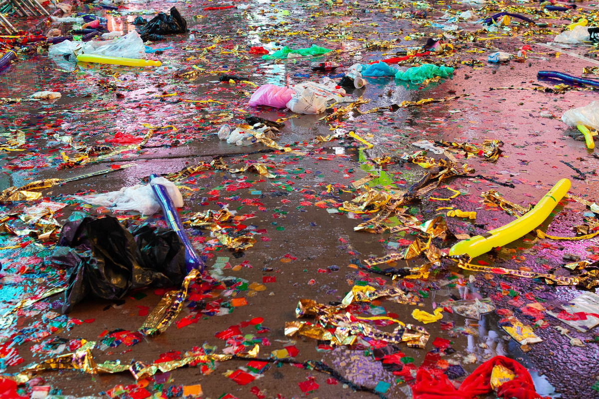 Image of the detritus of Times Square New Year's Eve featuring garbage and confetti on wet pavement.