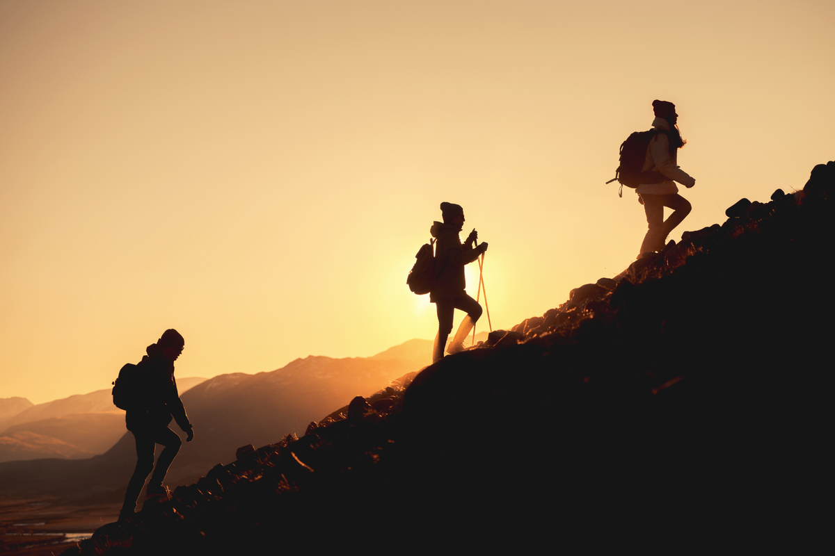 Image of three hikers climbing up an incline, silhouetted by a golden sunset.
