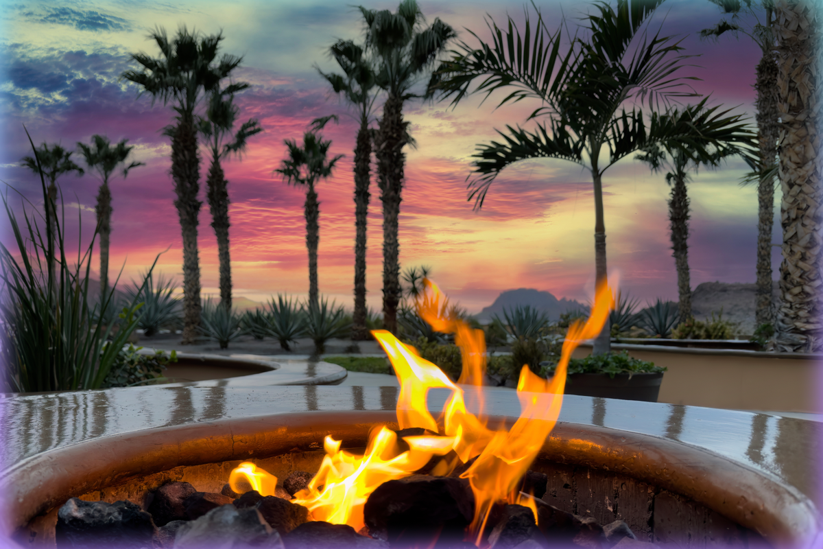 Image of a firepit in the foreground and palm trees against a sunset in the background.
