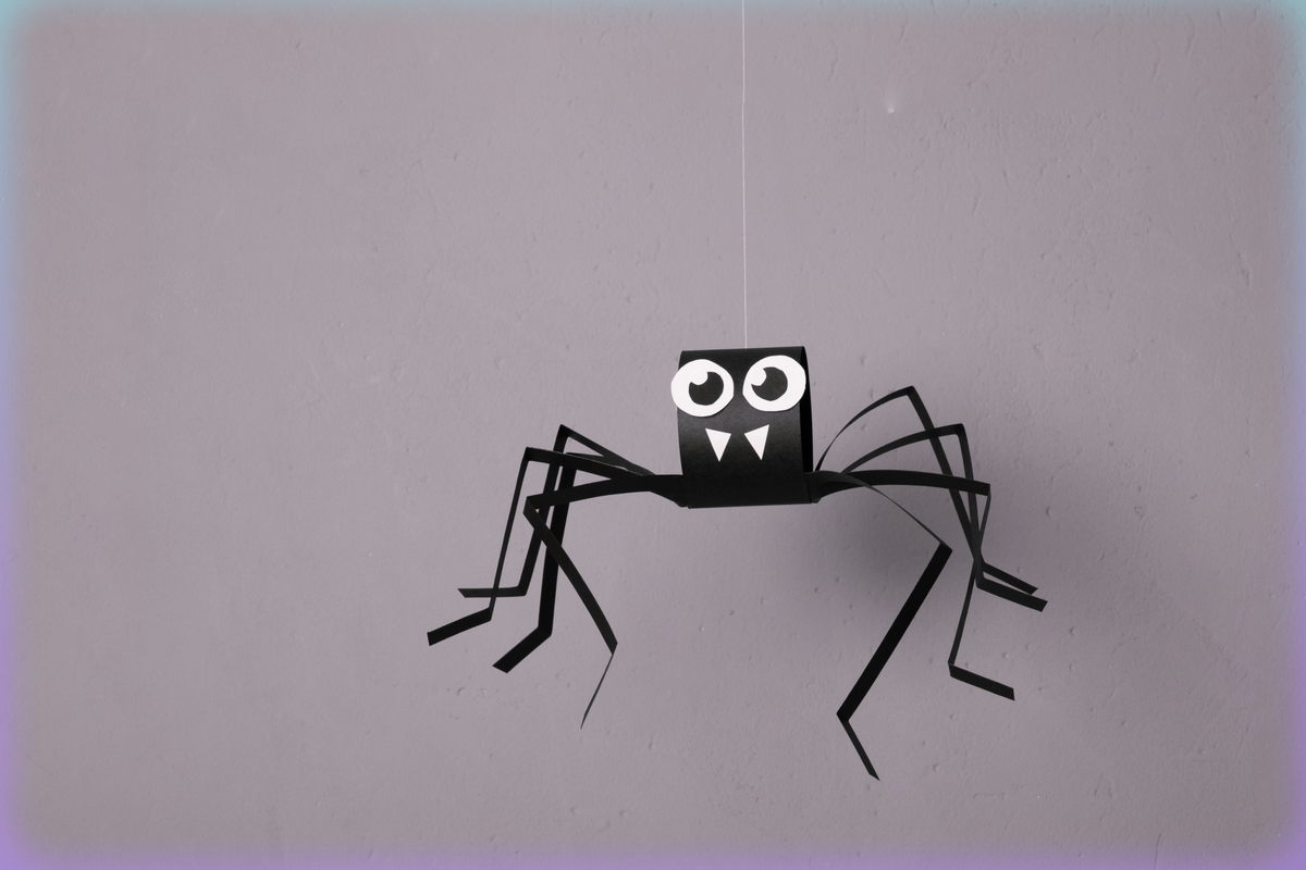 Image of a spider made of black construction paper with little white fangs and big plastic googly eyes, set against a grey background.