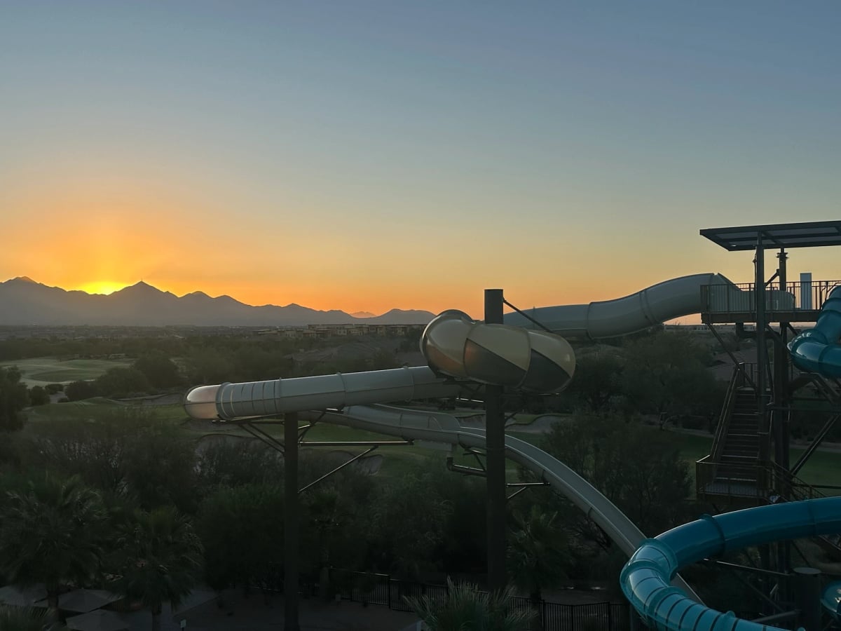 The sun rises over distant mountains—a beautiful desert scene. In the darker foreground a large looping water slide fills in half the frame on the right.