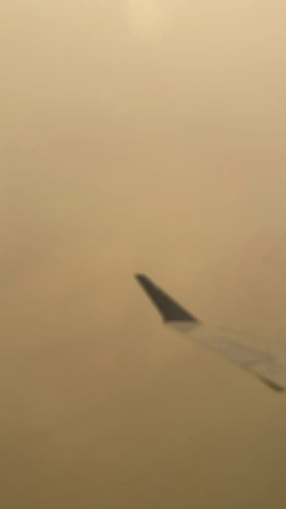 The tip of a plane wing over an orange gray sea of wildfire fog. Nothing else to see.