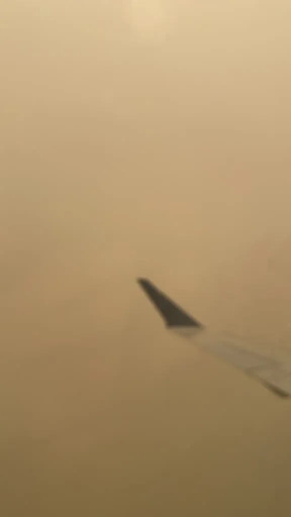The tip of a plane wing over an orange gray sea of wildfire fog. Nothing else to see.