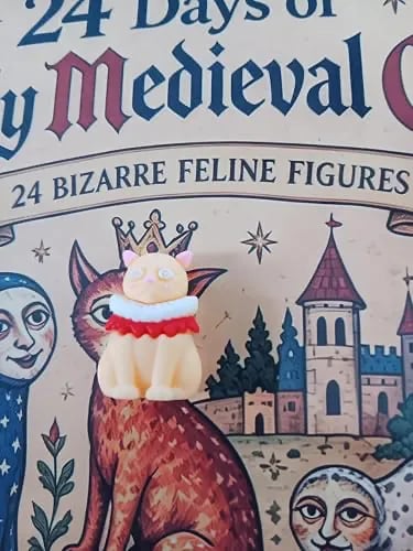 A shitty plastic cat, beige plastic with a red and white ruffle, and a strange stare, extremely undetailed.
